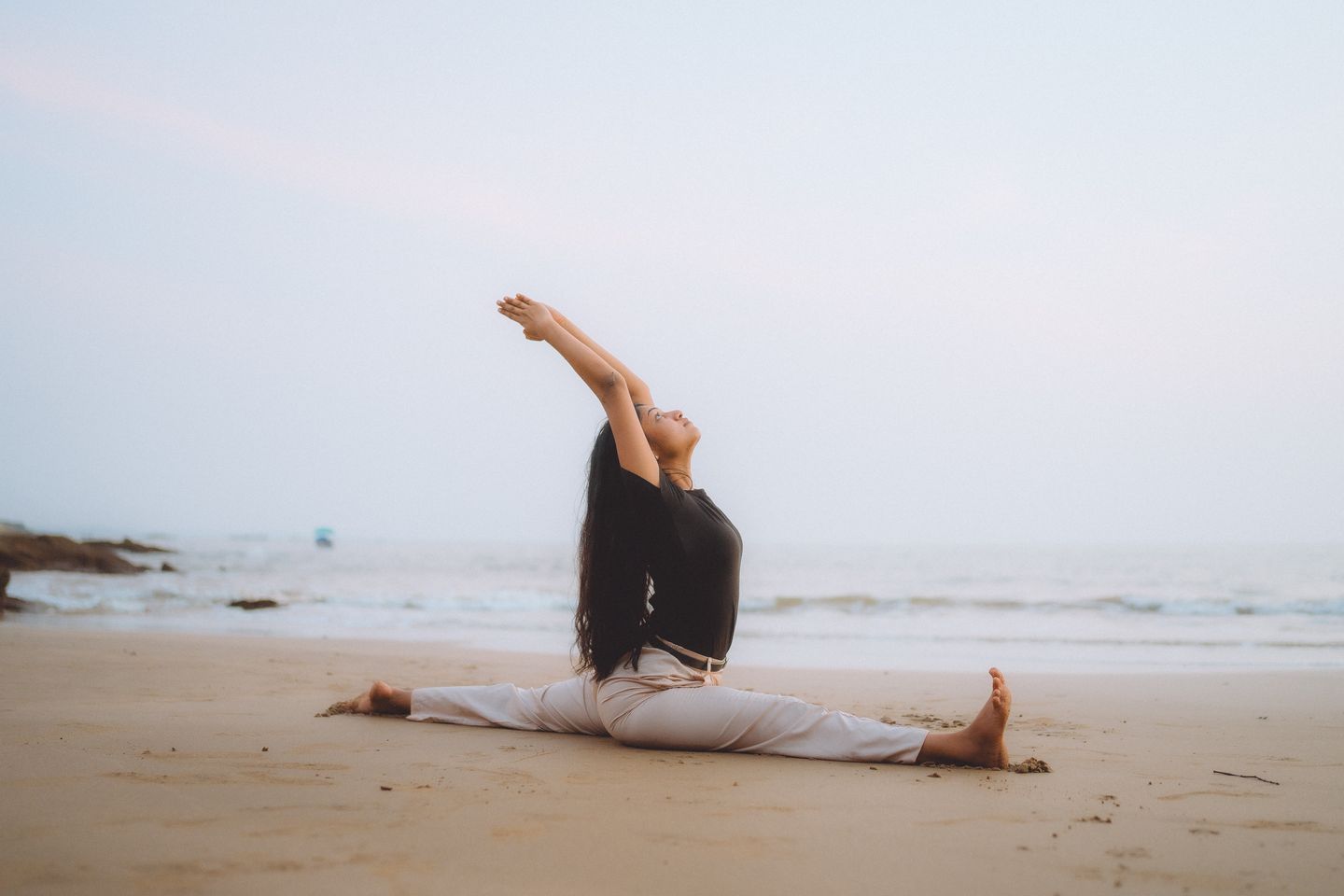 Serene beach yoga session at sunrise with woman performing splits, embodying calm and balance.
