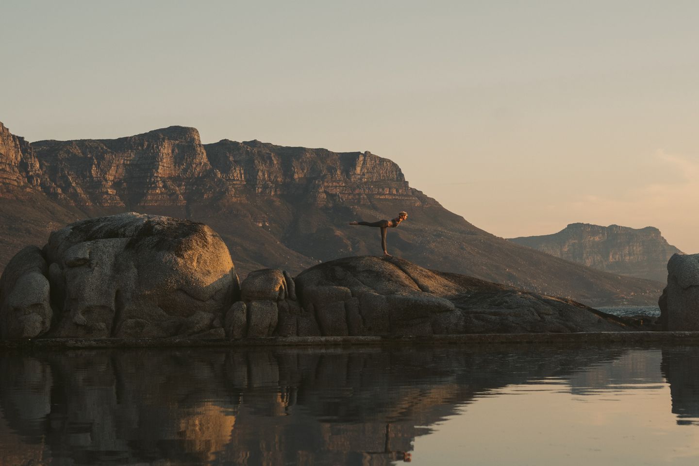 Woman practicing yoga on boulders during sunset in Cape Town, reflecting a serene wellness moment.